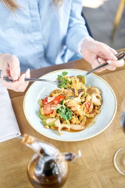 Kadın deniz ürünleri ve domates soslu İtalyan makarnayiyor. Makarna Gamberini. Yakın çekim tagliatelle bir kaşıkla bir çatal etrafında rüzgar. Parmesan peyniri