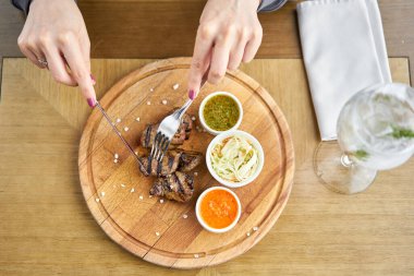 Bir restoranda öğle yemeği, bir kadın ızgarada pişmiş ciğer parçaları keser. Tahta bir tahtanın üzerinde hizmet veriyor. Barbekü lokantası menüsü, bir dizi farklı etin fotoğrafları..