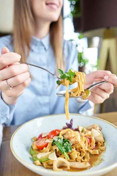 Woman eats Italian pasta with seafood and tomato sauce. Pasta Gamberini. Close-up tagliatelle wind it around a fork with a spoon. Parmesan cheese — Stock Photo, Image