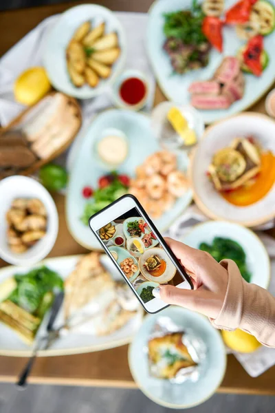 Bloger robi zdjęcie na smartfonie dla portali społecznościowych. Stół z talerzami owoce morza Bbq z dekoracji. Różnorodność potraw na stole. Menu restauracji. — Zdjęcie stockowe