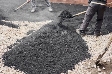 Yeni asfalt döşemek, çukuru kaplamak, molozların üzerinde. İşçiler kürek taşır ve pürüzsüz, sıcak asfalt için asfalt flüt kullanırlar..