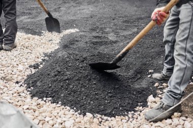 Yeni asfalt döşemek, çukuru kaplamak, molozların üzerinde. İşçiler kürek taşır ve pürüzsüz, sıcak asfalt için asfalt flüt kullanırlar..