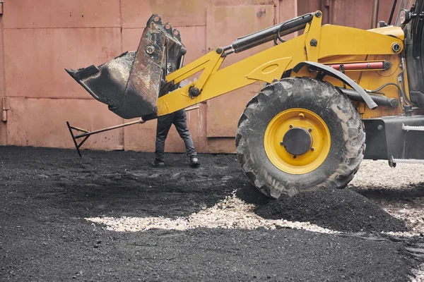 Een tractor laadt het asfalt uit. Grote zware machines voeren wegenreparatiewerkzaamheden uit. Ik leg nieuw asfalt. Aanleg van een nieuwe asfaltweg. — Stockfoto