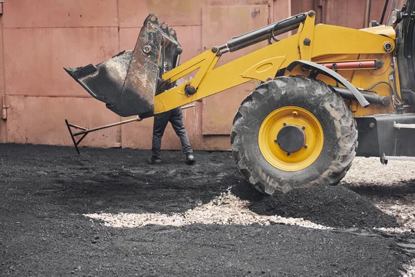 Un tractor descarga el asfalto. Gran maquinaria pesada está llevando a cabo trabajos de reparación de carreteras. Colocando asfalto nuevo. Construcción de una nueva carretera de asfalto . — Foto de Stock