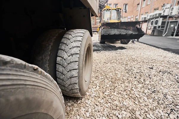 Ciągnik rozładowuje asfalt. Duże ciężkie maszyny wykonują prace remontowe. Układam nowy asfalt. Budowa nowej drogi asfaltowej. — Zdjęcie stockowe