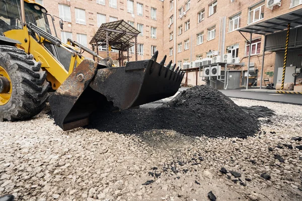 Ciągnik rozładowuje asfalt. Duże ciężkie maszyny wykonują prace remontowe. Układam nowy asfalt. Budowa nowej drogi asfaltowej. — Zdjęcie stockowe