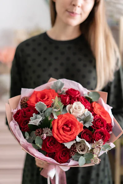 Buquê misto de tons vermelhos. Belo ramo de flores frescas em mãos de mulheres. O trabalho da florista em uma loja de flores. Flores frescas cortadas . — Fotografia de Stock