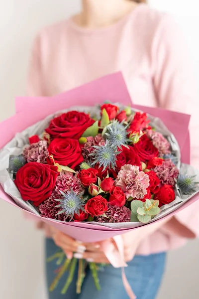 Buquê misto de tons vermelhos. Belo ramo de flores frescas em mãos de mulheres. O trabalho da florista em uma loja de flores. Flores frescas cortadas . — Fotografia de Stock