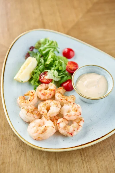 Délicieuses crevettes fraîches aux légumes frais et au citron vert. Assiette sur table en bois. Sauce à la crème — Photo