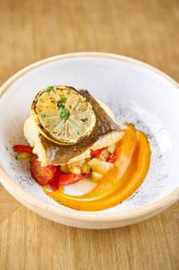 Kavrulmuş turna levrek veya pişmiş sebze ile morina balığı. Çanak limon bir dilim ile dekore edilmiştir. Restoran menüsü