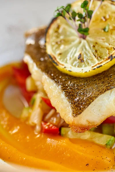Närbild Rostad gös eller torskfisk med bakade grönsaker. Dish dekorerad med en skiva citron. Restaurang meny — Stockfoto