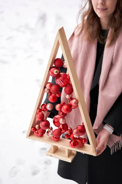 Альтернативна дерев'яна ялинка в руках жінок. Різдвяна ялинка ручної роботи та червоні різдвяні кульки . — стокове фото