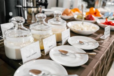 Önünde kaşıklar olan çay tabakları. Tatlım, konsantre süt, yoğurt. Otelde açık büfe kahvaltı..