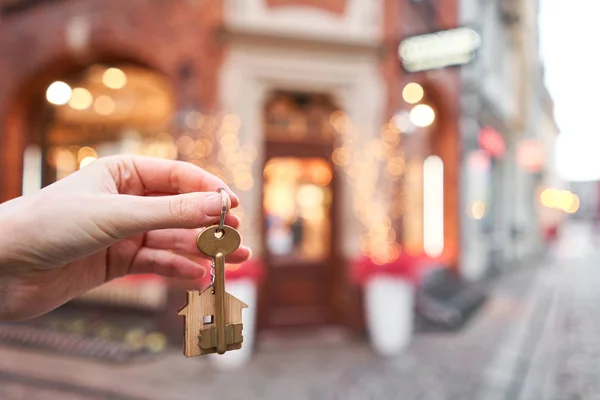 Concepto de hipoteca o alquiler. Mujeres sosteniendo la llave con llavero de la casa de madera. Bienes raíces, hipotético, mudarse a casa o alquilar una propiedad. Humor navideño en un fondo borroso. — Foto de Stock