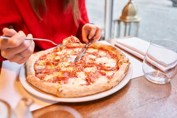 Frau isst mit Messer und Gabel eine Pizza capricciosa. Pizza mit Mozzarella-Tomaten, Artischocke, schwarzen Oliven und Basilikum Neapolitanische Pizza aus dem Holzofen. Mittagessen in einem italienischen Restaurant. — Stockfoto