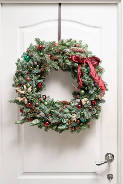 Όμορφο χριστουγεννιάτικο στεφάνι από φρέσκο έλατο στη λευκή πόρτα. Είσοδος στο σπίτι. Χριστουγεννιάτικη διάθεση. Χριστουγεννιάτικο δέντρο. — Φωτογραφία Αρχείου