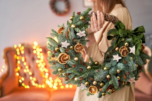 Noel havası. Kadın ellerinde taze ladin çelengi var. Xmas ağacı. Arka planda çelenk ışıkları Bokeh. — Stok fotoğraf