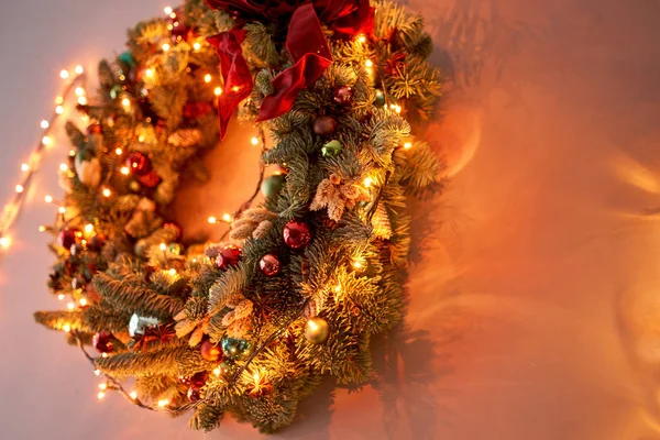 Closeup Beautiful festive wreath of fresh spruce on the gray wall. Christmas mood. Xmas tree. Bokeh of Garland lights on background. — Stock Photo, Image