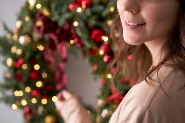 Piękny świąteczny wieniec ze świeżego świerku w kobiecych rękach. Krążek świąteczny z czerwonymi i złotymi ozdobami i kulkami. Boże Narodzenie. Szara ściana na tle. — Zdjęcie stockowe