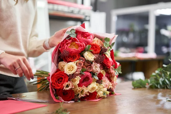 Step by step florist woman creates red beautiful bouquet of mixed flowers. Handsome fresh bunch. Education, master class and floristry courses. Flowers delivery. European floral shop concept.