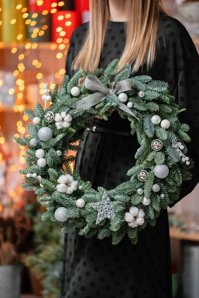 美丽的节日花环,新鲜的云杉在女人的手中. 圣诞气氛。 背景上加兰灯的Bokeh. — 图库照片