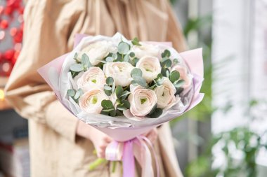 Kadınların elinde İranlı düğün çiçeği. Yeşil okaliptüslü soluk pembe ranunculus çiçekleri. Çiçekçi dükkanındaki çiçekçinin işi.