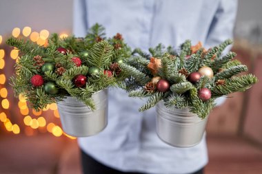 Metal bir tencerede iki küçük taze ladin aranjmanı. Noel havası. Arka planda çelenk ışıkları Bokeh.