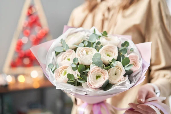 Persian buttercup in womans hands. Bunch pale pink ranunculus flowers with green eucalyptus. The work of the florist at a flower shop