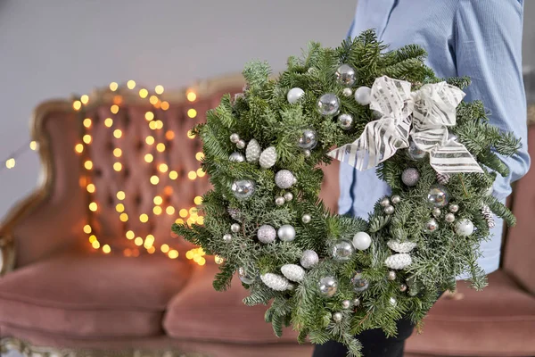 Kerststemming. Prachtige feestelijke krans van verse sparren in vrouwenhanden. Kerstboom. Bokeh van Garland lichten op de achtergrond. — Stockfoto