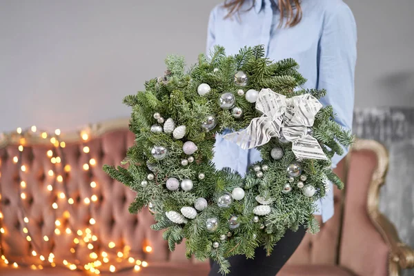 Karácsonyi hangulat. Gyönyörű ünnepi koszorú friss lucfenyővel a női kezekben. Karácsonyfa. Bokeh of Garland fények a háttérben. — Stock Fotó