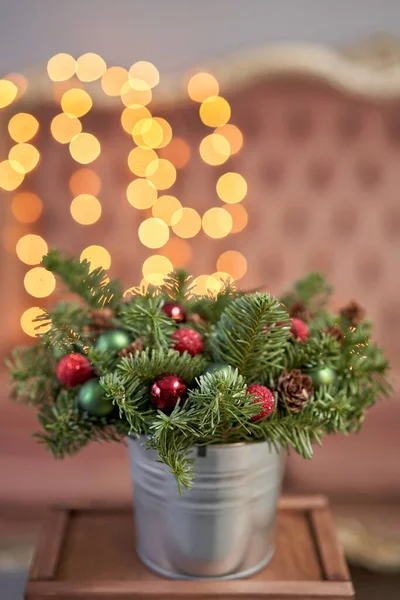 Pequeno acordo de abeto fresco em um pote de metal. Humor de Natal. Bokeh de luzes de guirlanda no fundo . — Fotografia de Stock