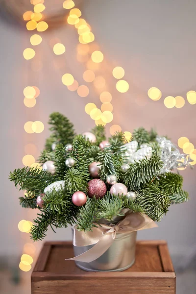 Pequeno acordo de abeto fresco em um pote de metal. Humor de Natal. Bokeh de luzes de guirlanda no fundo . — Fotografia de Stock