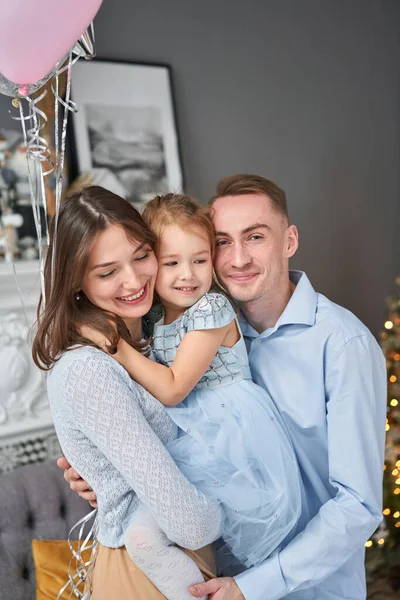 Sevgi dolu aile. Anne ve baba küçük kızına sarılıyor. Ebeveynler ve bebek çocuklar Noel ağacı ve beyaz şöminenin yanında eğleniyorlar. Mutlu Noeller ve mutlu yıllar. Neşeli güzel insanlar.. — Stok fotoğraf