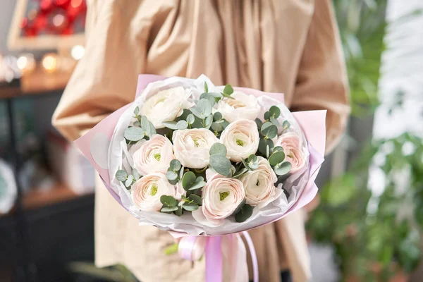 Περσικό βουτυρόκρεμα σε γυναικεία χέρια. Ένα μάτσο χλωμά ροζ λουλούδια ranunculus με πράσινο ευκάλυπτο. Η δουλειά του ανθοπώλη σε ανθοπωλείο — Φωτογραφία Αρχείου