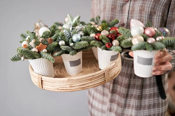 Florista segura uma bandeja com arranjos de Natal e um em sua mão. Belo arranjo festivo de abeto fresco na xícara de café. Humor de Natal . — Fotografia de Stock