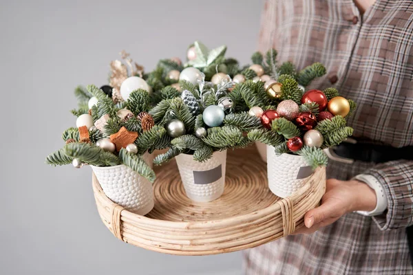 Kwiaciarnia trzyma tacę z przygotowaniami świątecznymi. Piękny uroczysty układ świeżego świerku w filiżance kawy. Świąteczny nastrój. — Zdjęcie stockowe
