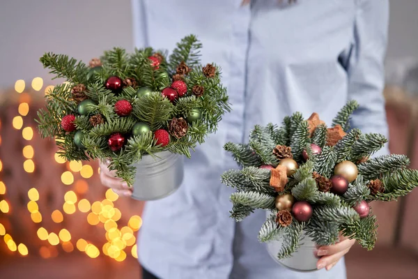 Twee kleine arrangementen van verse sparren in een metalen pot. Kerststemming. Bokeh van Garland lichten op de achtergrond. — Stockfoto