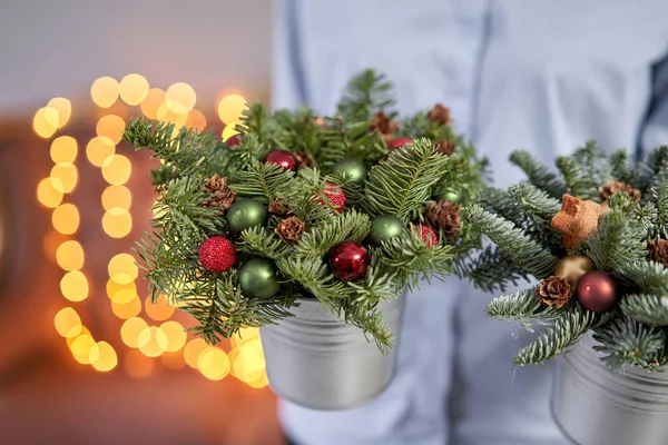 Twee kleine arrangementen van verse sparren in een metalen pot. Kerststemming. Bokeh van Garland lichten op de achtergrond. — Stockfoto