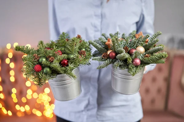 Twee kleine arrangementen van verse sparren in een metalen pot. Kerststemming. Bokeh van Garland lichten op de achtergrond. — Stockfoto