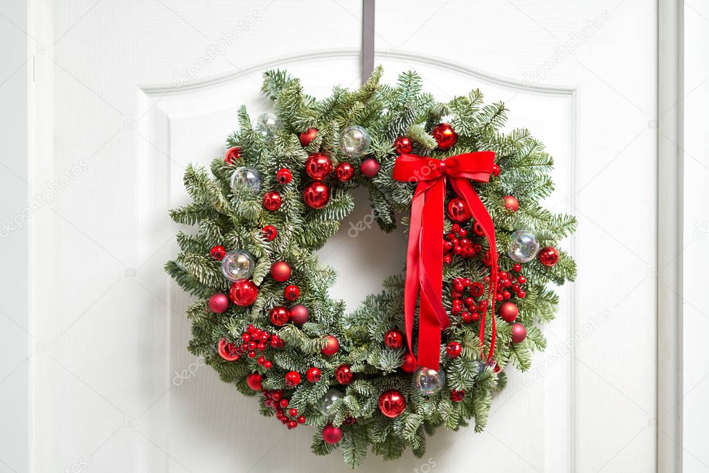 Beautiful red Christmas wreath of fresh spruce on the white door. Entrance to the house. Christmas mood. Xmas tree.