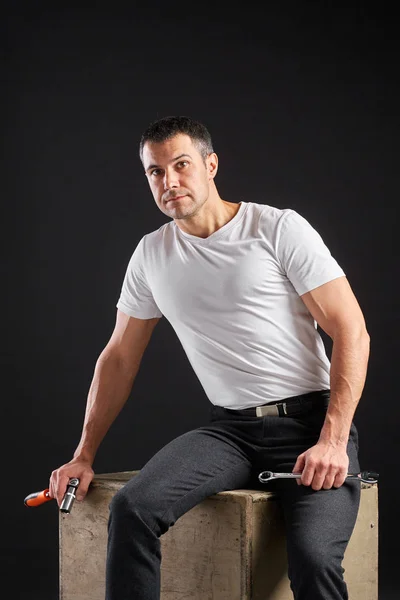 Atletisk man med skiftnyckel på svart bakgrund. Inte en typisk arbetare, i vit t-shirt och byxor. — Stockfoto