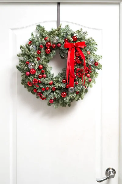 Όμορφο κόκκινο χριστουγεννιάτικο στεφάνι από φρέσκο έλατο στη λευκή πόρτα. Είσοδος στο σπίτι. Χριστουγεννιάτικη διάθεση. Χριστουγεννιάτικο δέντρο. — Φωτογραφία Αρχείου