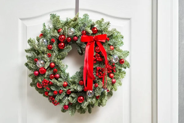 Gyönyörű vörös karácsonyi koszorú friss lucfenyővel a fehér ajtón. Bejárat a házba. Karácsonyi hangulat. Karácsonyfa. — Stock Fotó