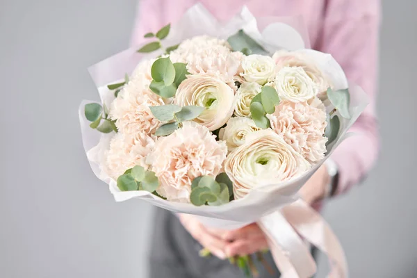 Butaca persa en manos de mujeres. Ramo de flores de ranúnculo rosa pálido con eucalipto verde. El trabajo de la floristería en una floristería — Foto de Stock
