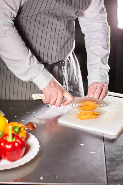 Closeup of hand with knife cutting fresh vegetable. Young chef cutting beet on a white cutting board closeup. Cooking in a restaurant kitchen.