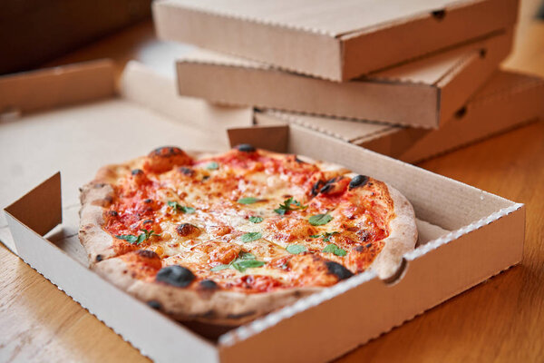 Pizza delivery concept. Baked products in a cardboard box against a wooden background. Baked tasty margherita pizza in Traditional wood oven in Neapolitan restaurant, Italy