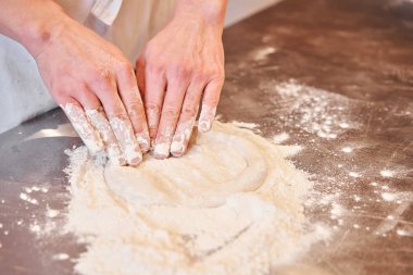 Napoli pizzası için hamur, şef kurusıkı mermi atıyor. Üniformalı beyaz önlüklü aşçının eli mutfakta pizza pişiriyor.