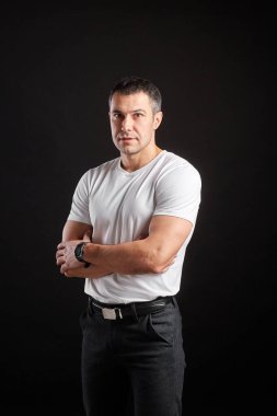 Beyaz tişörtlü yakışıklı atletik adam siyah duvar arkasında duruyor.