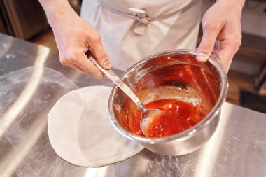 Pizza pişiriyorum. İşyeri domates sosu döktü. Şefin eli yakındır. Üniformalı fırıncı ve mutfakta beyaz önlüklü aşçı.