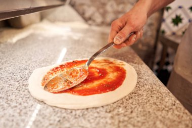 Pizza pişiriyorum. İşyeri domates sosu döktü. Şefin eli yakındır. Üniformalı fırıncı ve mutfakta beyaz önlüklü aşçı.